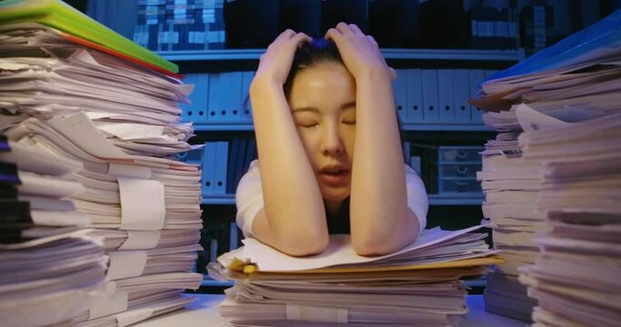 Young asian student woman dropping document on desk cover with stack of paperwork. Alone teen girl exhausted, tired and and lay down on pile of paper sheet while studying hard at late night.