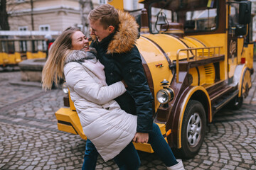 Man raises leg to woman, couple fooling around outdoors near yellow tourist bus