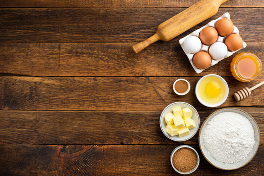 Cooking baking ingredients on a wooden table background. Flour eggs butter sugar and other pastry ingredients on wood. Top view copy space