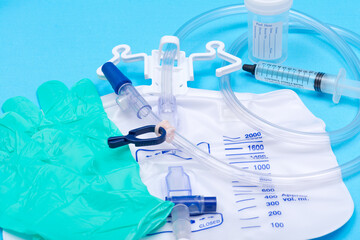 Fototapeta premium Sterile urinary drainage bag, 10 ml syringe pre-filled with sterile water and specimen container with lid and label. Isolated on blue background.