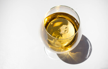 glass of white wine on white background with sparkling shadows. Free copy space.  Concept of luxury drinks. Top view.