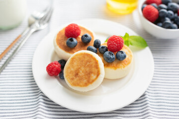 Syrniki, cottage cheese fritters served with berries on a white plate. Healthy breakfast food