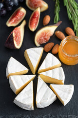 Camembert or brie cheese with figs, honey and almonds on black slate board