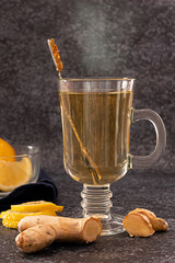 A glass of hot steaming ginger and lemon tea on dark background