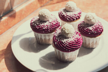 Four delicious cupcake with violet cream decorated with balls topped with coconut crumbs