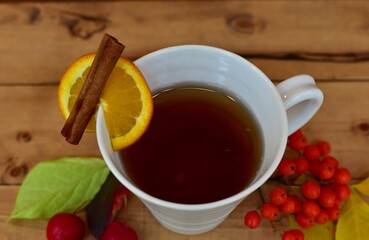 Warm cozy hot beverage in white mug with arranged autumnal decor of seasonal fall colourful leaves and berries to enjoy on cool autumn days