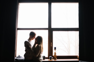 Portrait of a beautiful young couple at the window at home. A beautiful sunny morning of love and passion.