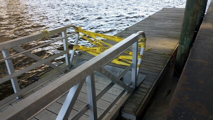 yellow cauton do not enter tape with wood pier and water