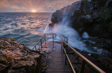 Stairs lead down to the sea with big waves and sunset in the background