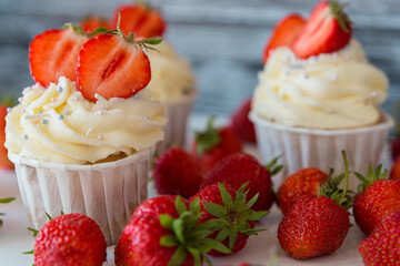 Delicious cupcakes with white cream decorated with ripe strawberries on a gray blue background.