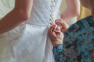 Mother of the bride helps to lace up the dress at the back
