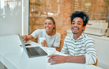 A beautiful woman and an attractive African man are drinking coffee in a coffee shop, working on a laptop, chatting and having fun.