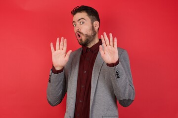 Young caucasian businessman wearing casual clothes standing over isolated red background Moving away hands palms showing refusal and denial with afraid and disgusting expression. Stop and forbidden.