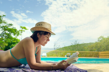 Woman reading and relaxing in luxury swimming pool. Relaxing vacation concept in swimming pool with...