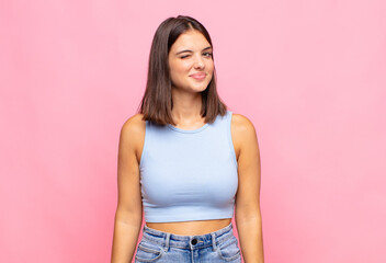 young pretty woman looking happy and friendly, smiling and winking an eye at you with a positive...