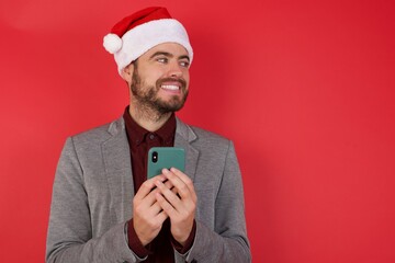 Young caucasian businessman wearing casual clothes standing over isolated red background hold telephone hands read good youth news look empty space advert