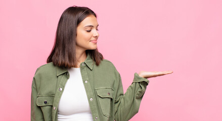 young pretty woman feeling happy and smiling casually, looking to an object or concept held on the...