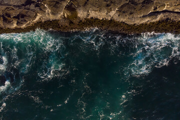 Obraz premium Aerial view of ocean waves and fantastic Rocky coast. Blue water background. The rocky coast is on top on the photo. Wallpaper. Raging ocean.