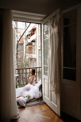 the morning of the bride. Girl in transparent dress on balcony, wedding dress hanging on the door