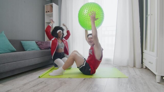 Funny retro style couple of Caucasian man and afro woman doing work up at home. Funny man doing abs exercises crunches at home with wife, fitness humor.