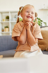 Vertical portrait of cute girl with down syndrome laughing happily while sitting on couch in sunlit...