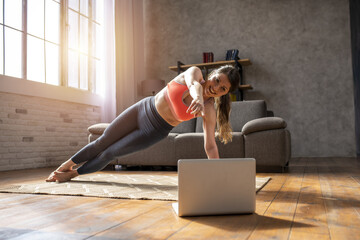 Young woman follows with a laptop a gym exercises. She is at home due to coronavirus codiv-19...