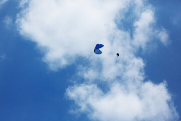 Blue Paraglider flying into the sky with clouds on a sunny day