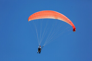 Blue Paraglider tandem instructor with a tourist flying into the sky with clouds on a sunny day