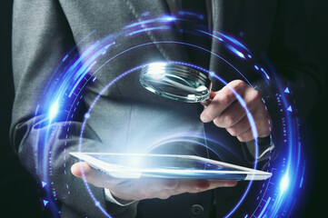 Businessman examines a tablet with a magnifying glass. Concept of internet security.