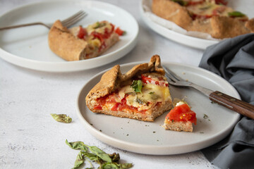 Slice of galette with tomatoes and cheese. Whole wheat rustic pie with tomatoes, cheeseand herbs. Healthy food concept.