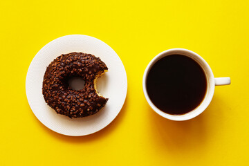 Breakfast concept. Morning coffee and bitten chocolate glazed donut with sprinkles on a bright...