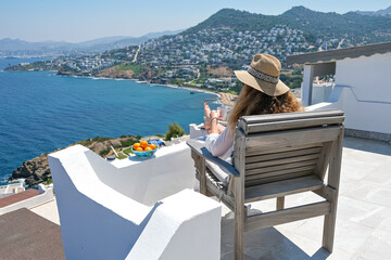 Beautiful young woman straw hat and coffee cup sitting on white terrace balcony of house or hotel with Sea View
