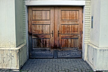 one large old brown wooden door on a gray concrete wall of a building on the street