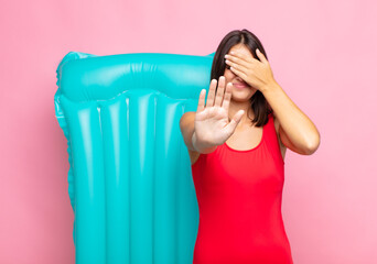 young pretty woman covering face with hand and putting other hand up front to stop camera, refusing...