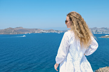 Fototapeta na wymiar Beautiful woman from back in white dress sunglasses on white terrace of villa hotel resort looking at Sea View