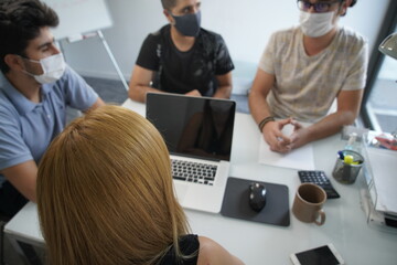 Teamwork Of Business People During Pandemic Of Coronavirus, Colleagues In Protective Masks Communicate Sitting At Negotiating Table In Office, Selective Focus On Smiling  Woman Using Computer