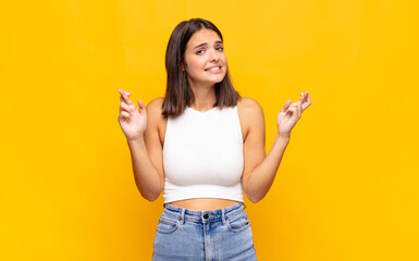 young pretty woman crossing fingers anxiously and hoping for good luck with a worried look