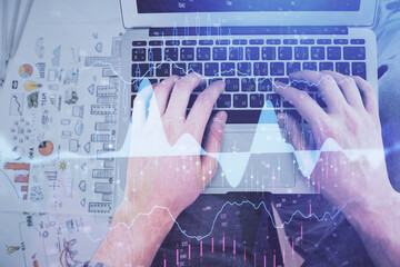 Double exposure of man's hands typing over laptop keyboard and forex chart hologram drawing. Top view. Financial markets concept.