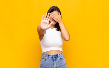 young pretty woman covering face with hand and putting other hand up front to stop camera, refusing...