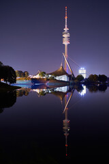 Munich skyline at night reflecting in a lake in the Olympiapark.