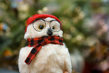 Toy owl with glasses and scarf on the background of the Christmas tree