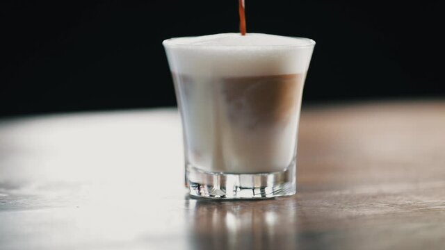Close-up of hot coffee being poured in a glass with hot milk and foam. Barista preparing a latte macchiato in slow motion
