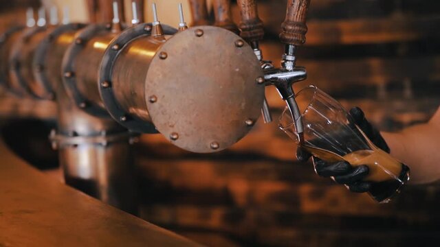 Bartender is pouring a dark stout beer in slow motion. Beer is poured from a metallic industrial style tap in a pub
