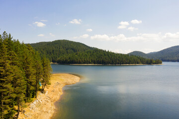 Beautiful lake, mountain peaks in light fog, aerial view from drone. Coniferous forests on banks of...