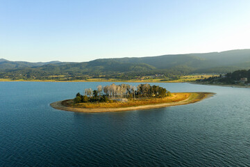 Beautiful lake, mountain peaks in light fog, aerial view from drone. Coniferous forests on banks of...