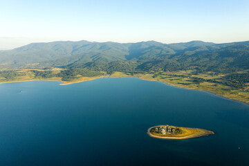 Beautiful lake, mountain peaks in light fog, aerial view from drone. Coniferous forests on banks of...