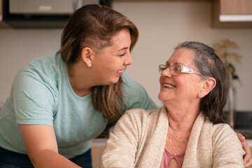 Portrait of latin grandmother and granddaughter looking to each other at kitchen table, inside. Relationship, leisure, domestic life, family concept..