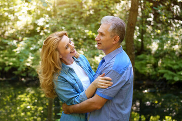 Mature happy couple stand in the forest on a sunny day and hug