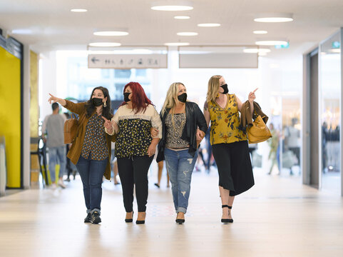 Shopping at the time Corona Virus with middle-aged Curvy Girls. Fashion group of Plus Size women friends at the shop center walking with protective surgical face mask and looking at shop windows.
