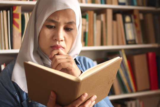 Asian muslim woman wearing hijab reading book in library, educational concept. Happy smiling expression, doing leisure activity